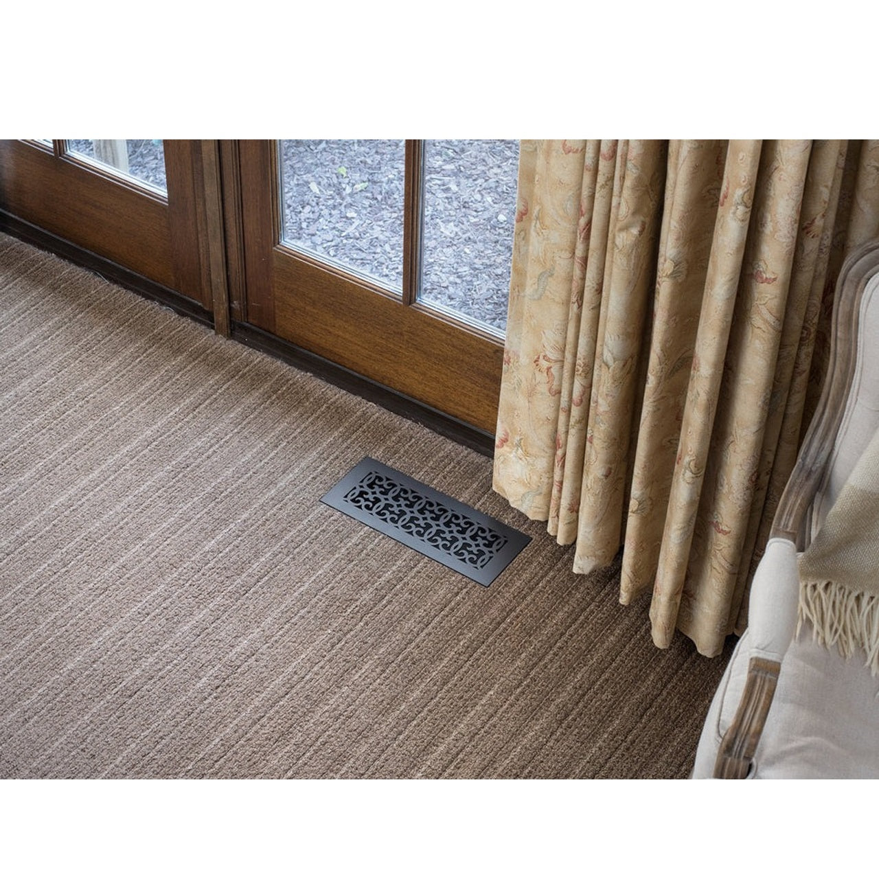 Versailles style vent cover in carpet next to a French door with gold drapes.